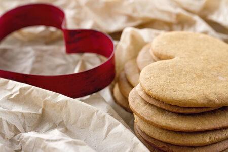 Red heart shaped cookie cutter and a pile of brown homemade Christmas gingerbread cookiesの写真素材