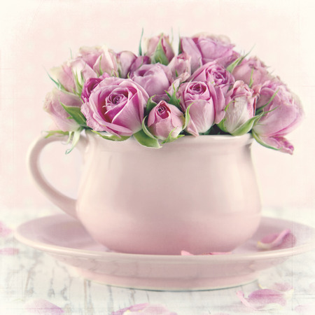 Bouquet of roses in a pink cup on wooden background with vintage textured editingの写真素材
