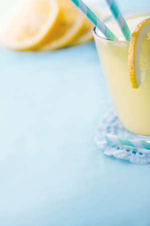 Glass of lemon juice on light blue background with hazy vintage editing