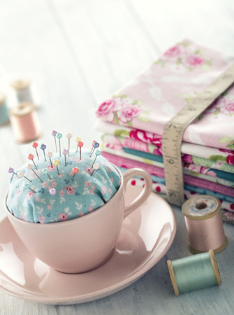 Green handmade floral pincushion in a pink cup with old spools of thread, sewing concept backgroundの写真素材