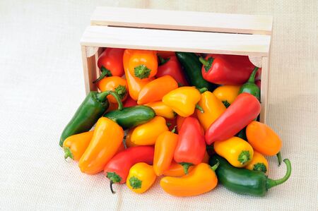 orange, yellow and red sweet peppers on wooden crate on burlap backgroundの写真素材