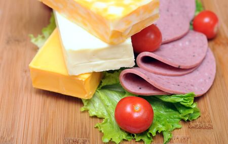 cheese, ham, and vegetables on bamboo cutting boardの写真素材