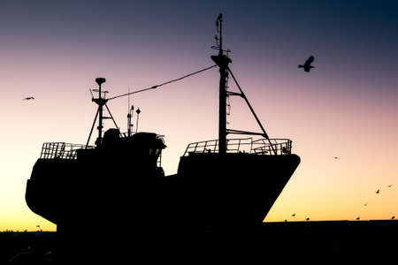 Fishing vessel silhouette at sunset in port, Essaouira, Moroccoの写真素材
