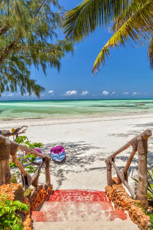 Way to the white sand tropical beach with boats under palm tree leaves at the shore of Indian ocean, Zanzibar, Tanzaniaの写真素材