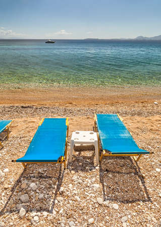 Empty beach Lounge chairs under bright sunlight at the shore of Ionian sea near Ipsos beach, Corfu, Greeceの写真素材
