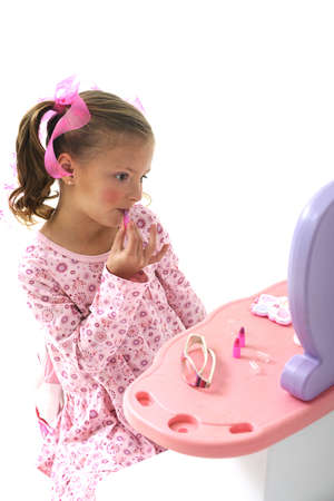 young pretty blond girl putting make-up on her face while sitting at a play setの写真素材