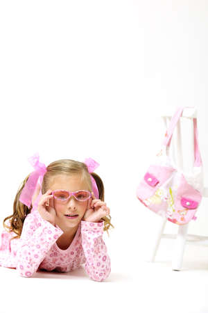 young pretty blond girl with sunglasses, laying on the floor next to a white chair and pink hand bagの写真素材
