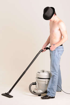 young man doing work at home with a vacuum cleaner without a shirt onの写真素材