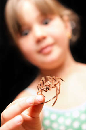 a pretty young girl wearing green polka dot dress holding a brown spider by the one leg and looking surprisedの写真素材