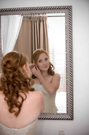red head sexy beautiful bride inserting her earrings in whilst smilingの写真素材