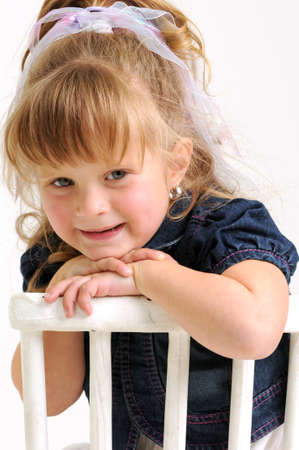 young pretty blond girl with blue dress sitting on a white chair and smilingの写真素材