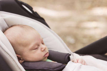 Baby boy fastened with security belt is sleeping peacefully in the car safety seat on the blur brown...