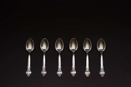 Six old silver spoons with ornament in a row on black background. Number concept
