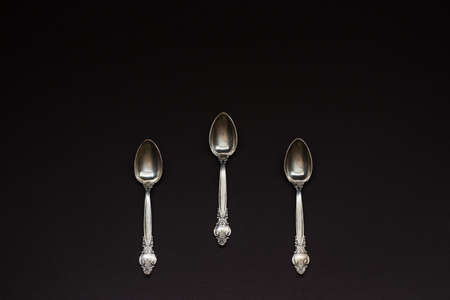 Three old silver spoons with ornament on black background. Number conceptの写真素材