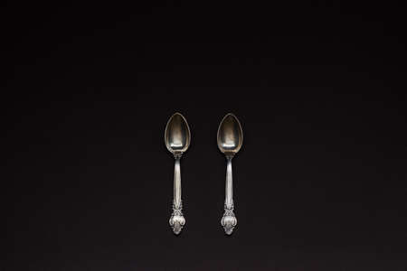 Two old silver spoons with ornament in a row on black background. Number conceptの写真素材