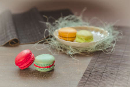 Traditional french macaroons, two on the table and two on the plate behind. Selective focus, vignette, pastel color filter usedの写真素材
