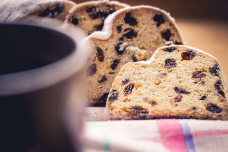 Stollen, traditional German Christmas yeast cake with raisins served with a cup of coffee, decorated with tablecloth on wooden table, selective focusの写真素材
