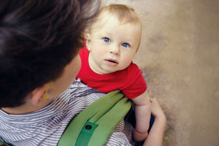 Stylish woman with short hair and wearing striped shirt, having her cute little son in baby carrier. View from the top and back. Traveling with baby concept. Space for your textの写真素材