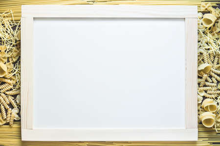 Mixed dried pasta selection surrounding white board with wooden frame for your text. Top view shotの写真素材