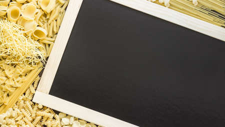Mixed dried pasta selection surrounding black board with wooden frame for your text. Top view shotの写真素材