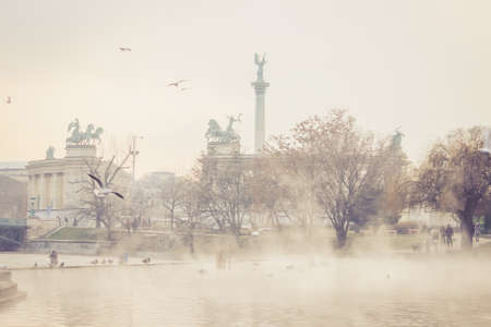 View on Heroes' Square (Hosok tere) from the City Park (Varosliget), a public park in Budapest, Hungary. Thermal water in the lake is steaming in foreground. Birds are flying above the lakeの写真素材