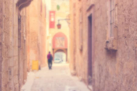 Defocused Background with Man walking down the Ancient narrow Street in Mdina, Malta. Warm color filter usedの写真素材