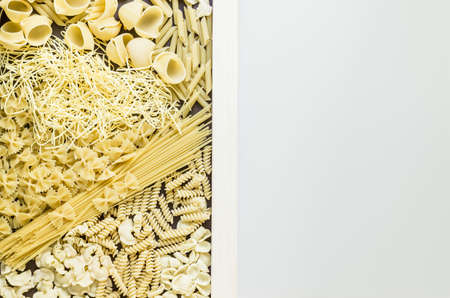 Mixed dried pasta selection surrounding white board and dividing photo in a half. Space for your text. Top view shotの写真素材