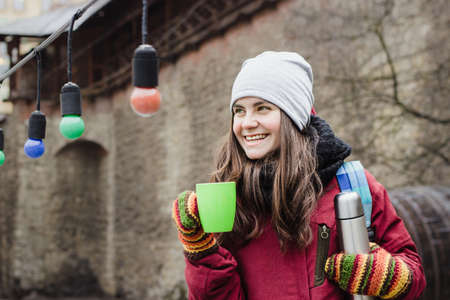 Young white woman with long brown hair, wearing red jacket, grey hat, black scarf and colorful mittens,の写真素材