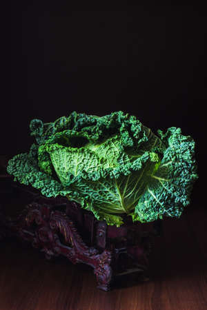 A whole head of leafy green Savoy cabbage on a beautiful vintage weight against a dark background. Vertical compositionの写真素材