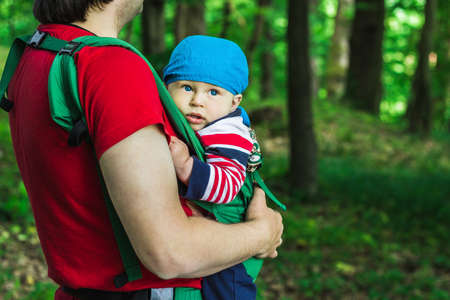 Father holding his son in baby carrier walking in the parkの写真素材