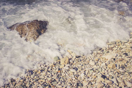 Foamy wave hits pebble rocks on the beach of the Adriatic Sea