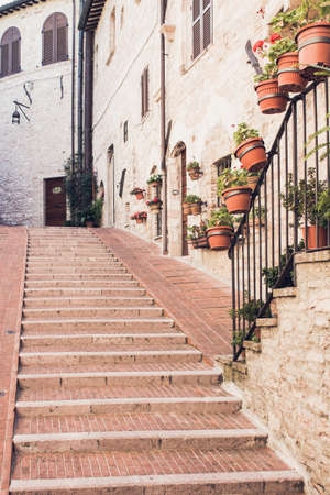 Narrow staircase street of the old town of Assisi with ancient stone houses decorated with flowerpots, Italyの写真素材