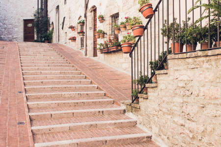 Narrow staircase street of the old town of Assisi with ancient stone houses decorated with flowerpots, Italyの写真素材