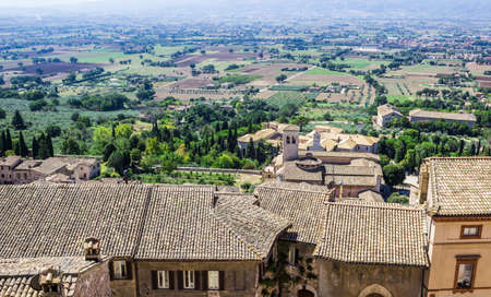 Panoramic view of beautiful typical italian fields landscape with roofs of the ancient town of Assisi on the foreground, Umbria, Italyの写真素材
