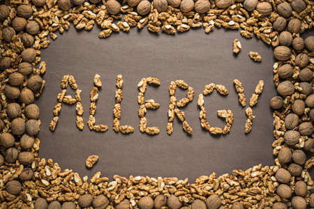 The word "allergy" is written from the walnuts on a dark brown paper background in a frame of walnuts. View from above. Allergy food conceptの写真素材