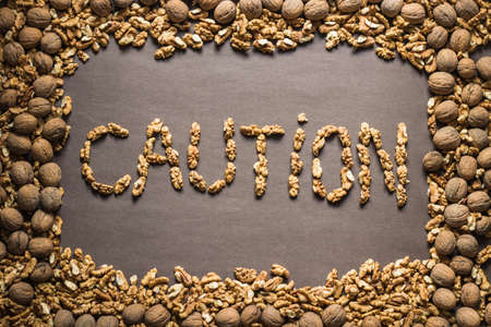 The word "caution" is written from the walnuts on a dark brown paper background in a frame of walnuts. View from above. Food allergy conceptの写真素材