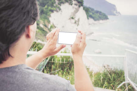 Young man holding smart phone with white empty screen in Numana, Marche, Italy. Travel conceptの写真素材