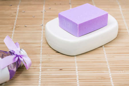 Bar of natural lavender soap on white ceramic soap dish and a bottle with shower gel over beige...