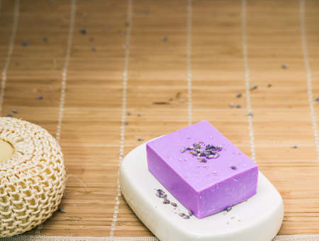Bar of natural lavender soap on white ceramic soap dish over beige bamboo mat backgroundの写真素材