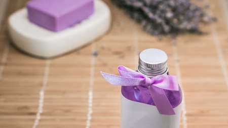 Bottle of natural lavender shower gel with purple ribbon over beige bamboo mat background