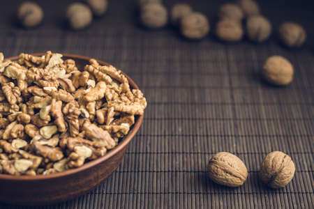 Walnut kernels and whole walnuts in brown ceramic bowl. Healthy organic food concept. Selective...