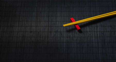 Yellow sushi chopsticks on black bamboo straw mat, space for textの写真素材