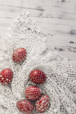 Decorated Easter eggs using a traditional in Eastern Europe wax-resist method and modern patterns. Still life with Pysanka, dry plants and lace on whitewashed wooden background, top view, copy spaceの写真素材