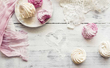 Zephyr (Russian marshmallow) on light wooden table covered with sugar powder and a heart drawn with finger. Top viewの写真素材
