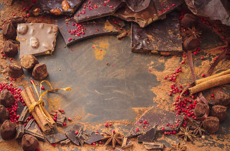 Assortment of chocolate bars, truffles, spices and cocoa powder on dark background