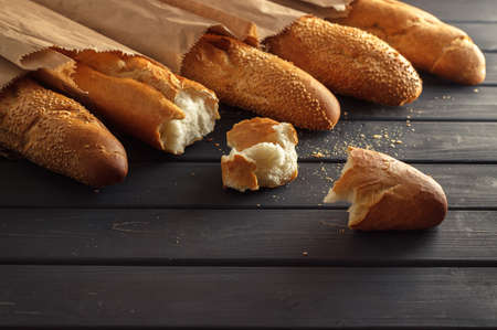 French baguettes with sesame seed in paper bags on black wooden background