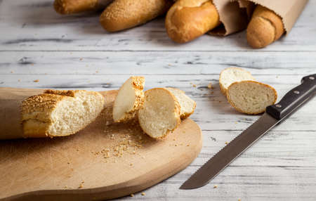 French baguette with sesame seed cut with a knife on cutting board on bright wooden backgroundの写真素材