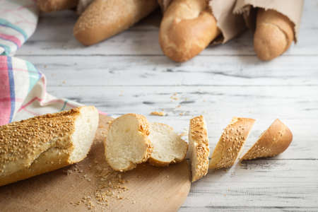 French baguette with sesame seed cut with a knife on cutting board on bright wooden backgroundの写真素材