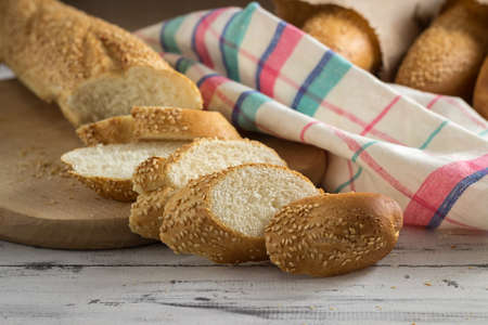 French baguette with sesame seed cut with a knife on cutting board on bright wooden backgroundの写真素材