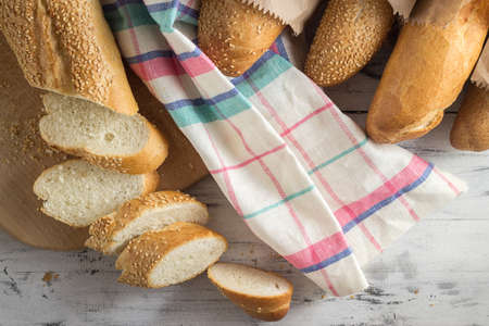 French baguette with sesame seed cut with a knife on cutting board on bright wooden backgroundの写真素材